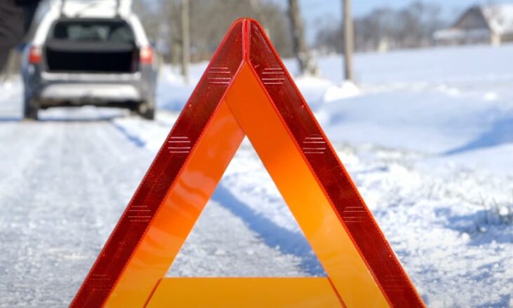 Reflective warning triangle placed on icy road with disabled vehicle in background